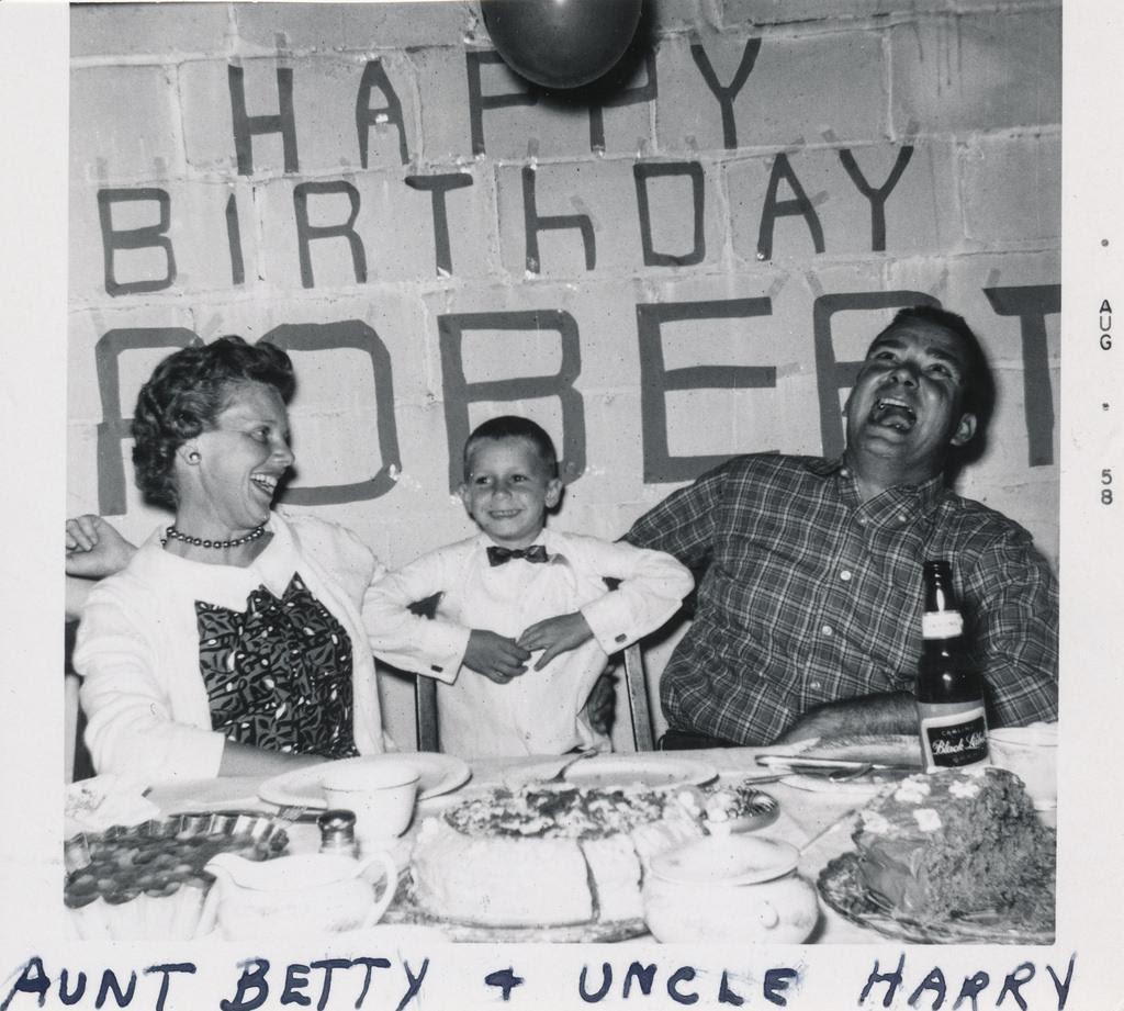 family birthday snapshot from the 1950s with Happy Brithday Robert spelled in large, awkward letters on the wall