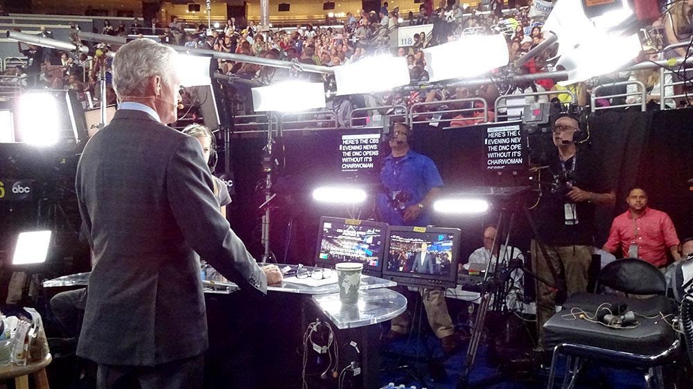 newscaster faces a bank of cameras and lights during Democratic National Convention